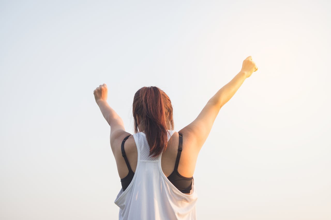 about-img A woman celebrates success with arms raised in a bright outdoor setting.