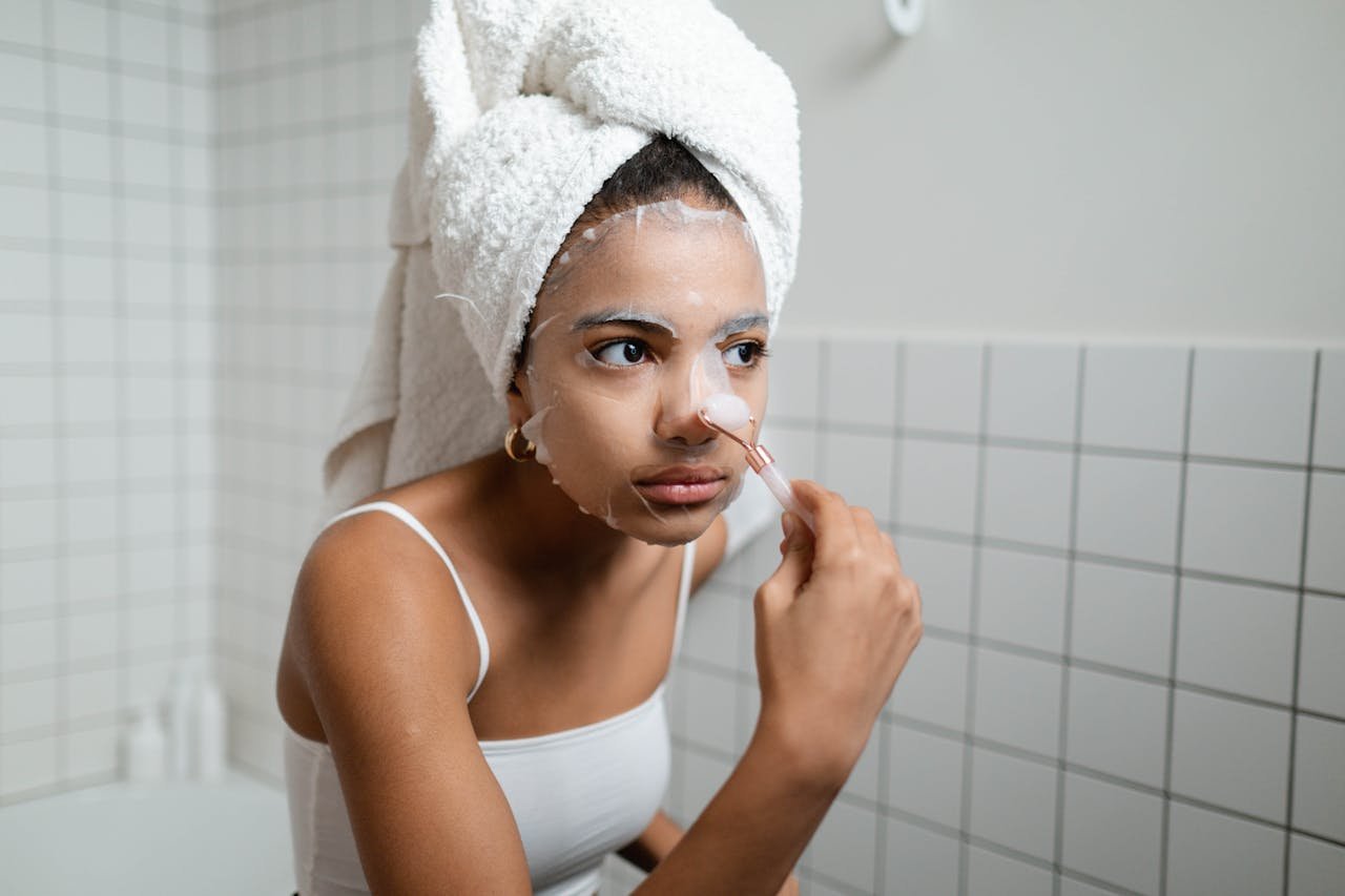 hero-gallery-02 A young woman applying a facial cosmetic mask in a modern bathroom, engaging in a beauty routine.